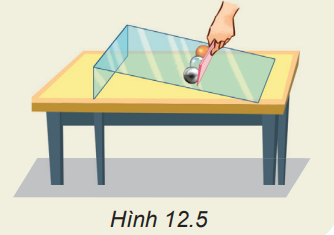 Dùng thước kẻ giữ ba viên bi (sắt, thủy tinh và gỗ) có cùng kích thước, trên một tấm thủy tinh đặt nghiêng trên mặt bàn rồi nâng thước lên (Hình 12.5). Hãy dự đoán tầm xa của ba viên bi và làm thí nghiệm kiểm tra. (ảnh 1)