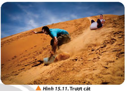 a) Phân tích các lực tác dụng lên hệ người và ván khi trượt từ trên đồi cát (Hình 15.11).   b) Phân tích đặc điểm của công do những lực này sinh ra trong quá trình trượt. (ảnh 1)