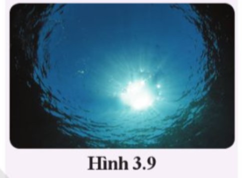 Khi người thợ lặn dưới nước nhìn lên trên chỉ thấy có một vùng hình tròn sáng ở mặt nước, phía ngoài vùng đó bị tối đen mặc dù bên trên không có vật che sáng (hình 3.9) Em hãy giải thích hiện tượng này. (ảnh 1)