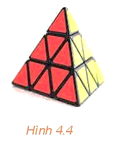 Trong Hình \(4.4\) là một khối rubik có bốn đỉnh và bốn mặt, mỗi mặt là một tam giác.   a) Đặt khối rubik sao cho ba đỉnh của mặt màu đỏ đều nằm trên mặt bàn.  (ảnh 1)